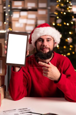Foto de Retrato del administrador sosteniendo el ordenador tableta con vacío en blanco. Santa trabaja en un almacén con paquetes con pedidos listos para su envío. concepto de venta de Navidad - Imagen libre de derechos