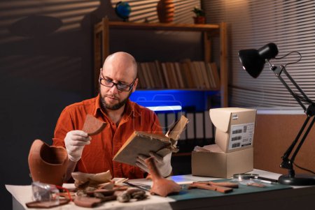 Foto de Arqueólogo trabajando hasta tarde en la noche en la oficina estudiando con libro. Primer plano - Imagen libre de derechos
