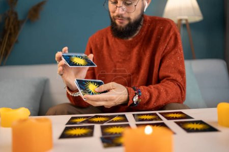 Young male fortune-teller with tarot cards recording video for blog at home. Copy space