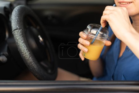 Téléchargez les photos : Femme boire du jus d'orange en voiture profiter du voyage, des vacances et du voyage sur la route. Espace de copie - en image libre de droit