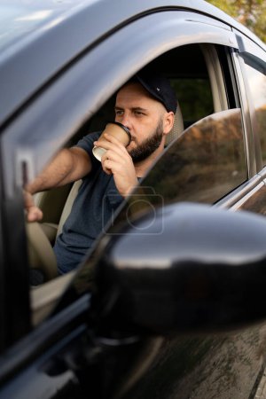 Photo for Bearded man drinking coffee while driving his car. Making a coffee break. Copy space - Royalty Free Image