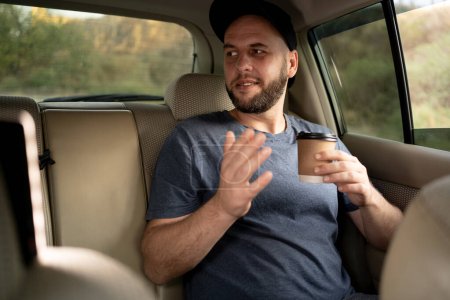 Téléchargez les photos : Passager masculin buvant du café à emporter et appréciant voyager en taxi. Concept de transport, véhicule et personnes - en image libre de droit