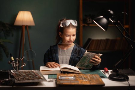 Téléchargez les photos : Circuit informatique de soudure écolière avec fer à souder et livre de lecture dans sa chambre à la maison. Espace de copie - en image libre de droit