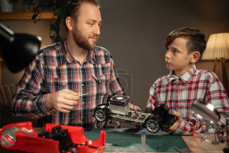 Photo for Young father teaching his son for soldering electrical car at home. Man and boy fixing broken toy. Copy space - Royalty Free Image