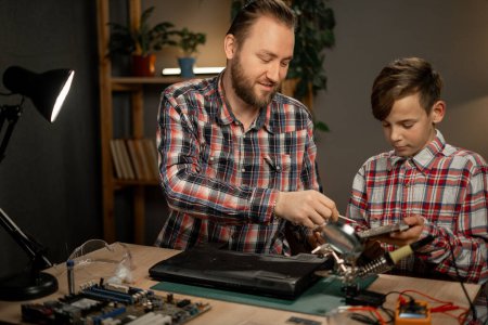 Photo for Father with son using soldering iron for repairing laptop computer at home. Concept of maintenance and family. Copy space - Royalty Free Image