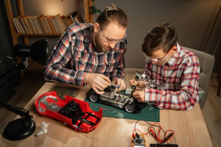 Téléchargez les photos : Père avec fils en utilisant du fer à souder pour réparer la voiture jouet à la maison. Famille et convivialité. Espace de copie - en image libre de droit