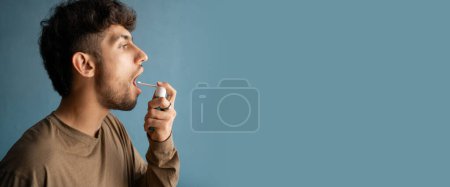 Téléchargez les photos : Jeune homme arabe utilisant pulvérisation de la gorge isolé sur fond bleu. Bannière. espace de copie - en image libre de droit