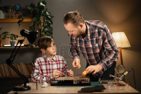 Téléchargez les photos : Père enseignant à son fils à réparer un ordinateur portable à la maison. Un jeune homme avec un garçon passe du temps ensemble. Espace de copie - en image libre de droit
