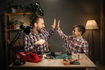 Photo for Teen boy giving high five to his father after fixing of electronic toy car. Concept of educational process. Copy space - Royalty Free Image
