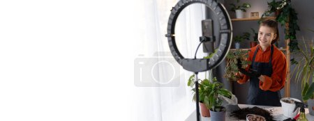 Photo for Child girl blogger blogging about houseplants, filming herself with flower on a smartphone on a stabilizer tripod. Banner. Copy space - Royalty Free Image