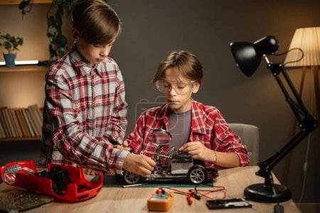 Photo for Brothers soldering wires for machine at home in the evening. Children studying technology and electronics in the workshop. Copy space - Royalty Free Image
