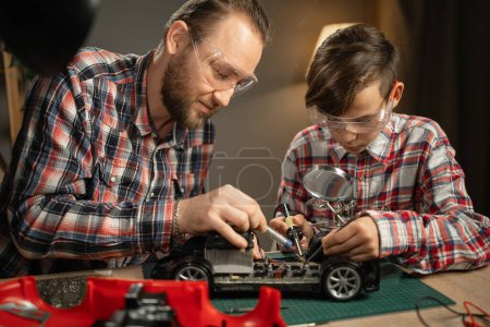 Photo for Father teaching his son for soldering and repair remote controlled car at home. Man and boy fixing broken toy. Copy space - Royalty Free Image