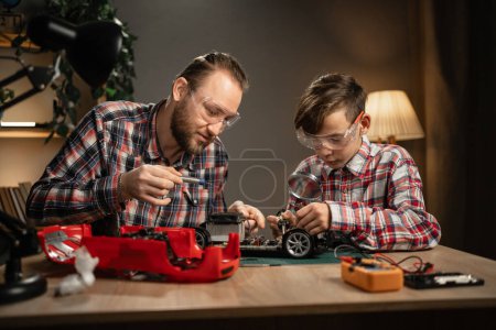 Photo for Father with son using soldering iron for repairing toy car at home. Family and togetherness. Copy space - Royalty Free Image