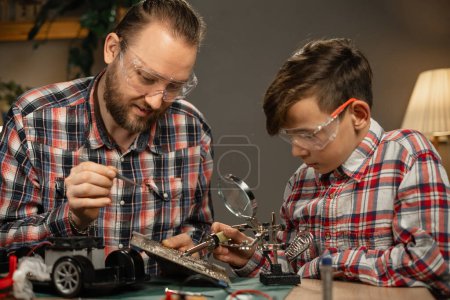 Photo for Concept of parenthood and educational process. Teen boy with his father fixing of remote controlled toy car. Copy space - Royalty Free Image