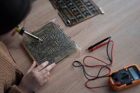 Photo for Schoolgirl soldering a component sitting at home in the evening, close-up. study online lesson excited make AI circuit toy. Copy space - Royalty Free Image