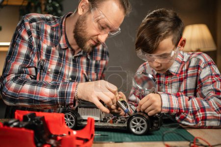 Photo for Father teaching his son for soldering and repair remote controlled car at home. Man and boy fixing broken toy. Copy space. - Royalty Free Image