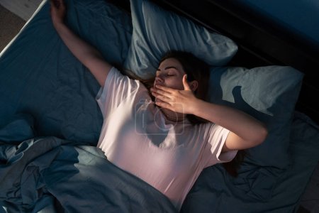 Mujer cansada cubriendo la boca y bostezando mientras yacía en la cama por la noche en casa. Copiar espacio