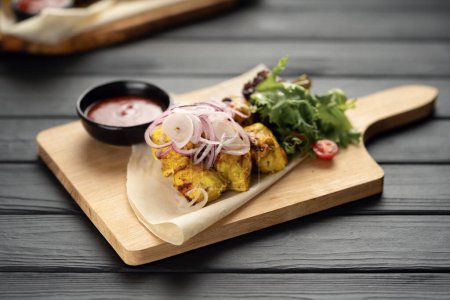Foto de Kebab de pollo a la parrilla servido con pan de pita y cebollas en escabeche en una tabla de madera. Concepto de picnic - Imagen libre de derechos