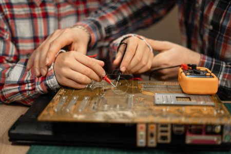 Photo for Close-up of father and son hands testing laptop motherboard using multimeter. DIY concept - Royalty Free Image