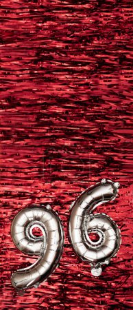 Foto de Globo de papel de plata número 96 sobre un fondo de decoración de oropel rojo. Tarjeta de felicitación de cumpleaños, inscripción 96. Evento de aniversario. Banner vertical. Copiar espacio - Imagen libre de derechos
