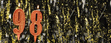 Burning red birthday candles on glitter tinsel background, number 98. Banner. Copy space