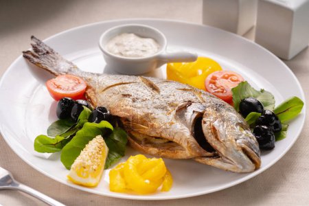 gegrillter Fisch dorada bbq mit Sauce, Tomaten und Zitrone auf weißem Teller. Ketogene Ernährung. Konzept für gesunde Ernährung.
