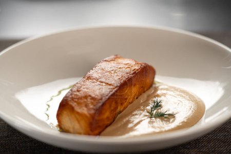 Ein Stück gebackener Lachs gegrillt mit zwei Saucen auf weißem Teller auf dem Tisch. Seitenansicht