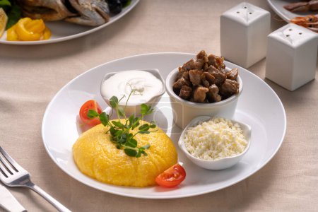 Téléchargez les photos : Délicieuse polenta au fromage, ragoût de viande et crème sure sur une assiette blanche servant sur table. Nourriture saine roumaine traditionnelle. Vue ci-dessus. - en image libre de droit