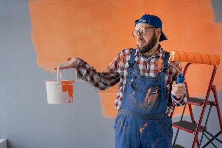 Männlicher Maler blickt angewidert auf einen Eimer Farbe. Kopierraum