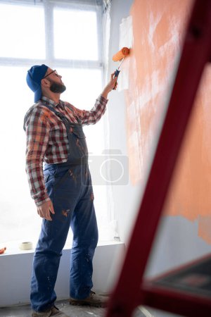 Photo for Male painter paints wall with painting roller. Repair, building and home concept. Side view. Copy space - Royalty Free Image
