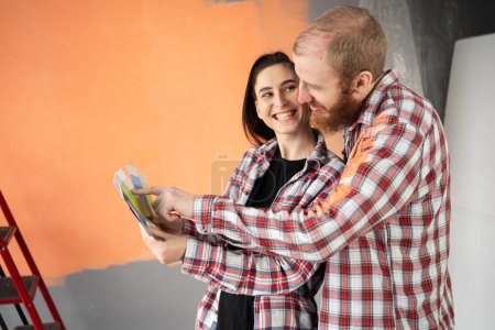 Happy young couple choosing paint colors from palette for new house. Room at home is prepared for renovations. Home, moving, decoration, renovation and wall painting concept.