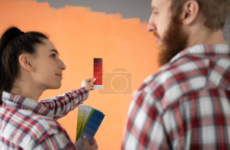 Home, moving, renovation and wall painting concept. Young couple choosing color with palette in their new house. Copy space