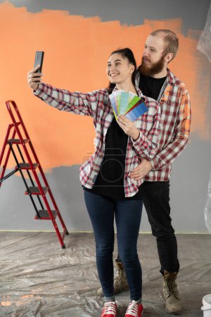 Pareja decorar casa y tomar selfie por teléfono móvil después de pintar la pared con color naranja. Copiar espacio