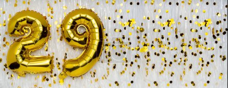 Foil balloon number and digit twenty-nine 29. Birthday greeting card. Golden balloons on white background with copy space. Numerical digit. Anniversary concept.