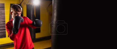 Concept sport. Strong athletic young man is training self-defense punches in boxing gloves. Banner. Copy space
