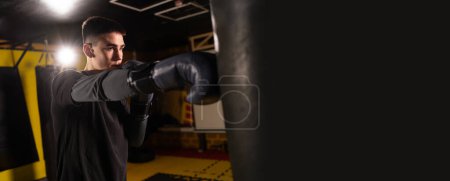 Young boxer workout a kick on punching bag in gym. Sport and active lifestyle concept. Copy space. Banner