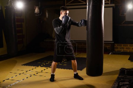 Full length view of young male boxer training with punching bag in he gym. Copy space