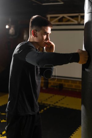 Téléchargez les photos : Un jeune boxeur frappe un sac de boxe dans un club de boxe. Beau boxeur homme s'entraînant dur. Espace de copie - en image libre de droit