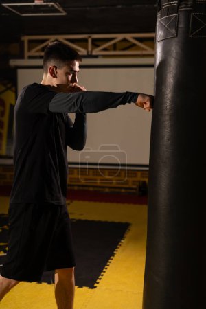 Téléchargez les photos : Boxe masculine boxe à l'entraînement sac de boxe dans la salle de gym sombre. Concept de sport de boxe. Vue verticale - en image libre de droit