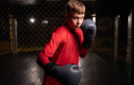 Téléchargez les photos : Jeune boxeur masculin confiant debout dans la pose et prêt à se battre dans la salle de gym, copier l'espace. Regardant la caméra - en image libre de droit
