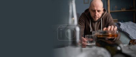 Sad depressed man drinking whisky at home sitting on sofa. Banner. Copy space