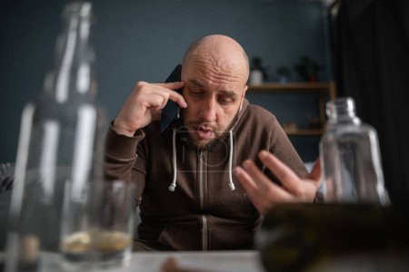 Téléchargez les photos : Boire du whisky alcoolisé masculin Boozy et appeler sur smartphone à la maison. Alcoolisme, dépendance à l'alcool et concept humain - en image libre de droit