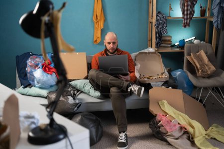 Hombre barbudo freelancer trabajando o estudiando en una habitación desordenada. Copiar espacio