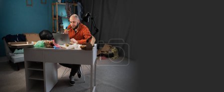 Un hombre freelance que trabaja en una habitación sucia y abarrotada come pizza en el almuerzo. Banner. Copiar espacio