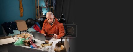 Man holding plastic credit card and using laptop sitting in messy room. Online shopping concept. Banner. Copy space