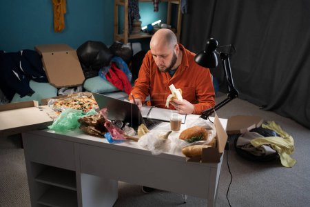 Photo for Adult serious male student working studying in messy room, making notes in his notepad - Royalty Free Image