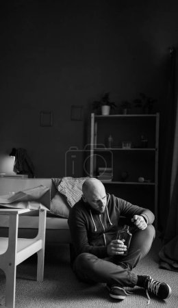 Konzept von Alkoholismus, Depressionen und Alkoholsucht. Unglücklicher einsamer Mann, der zu Hause Alkohol trinkt. Schwarz-Weiß-Foto. Kopierraum