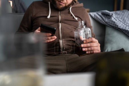 Téléchargez les photos : Gros plan de l'homme ivre avec smartphone buvant à la maison. Concept d'alcoolisme et de dépendance à l'alcool. - en image libre de droit