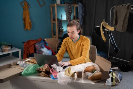 Young hipster male student working or studying in messy room in his home. Copy space
