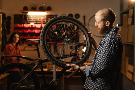 männlicher Arbeiter, der ein Rad hält und repariert, während er in einer Fahrradwerkstatt oder einer authentischen Garage steht. Kopierraum